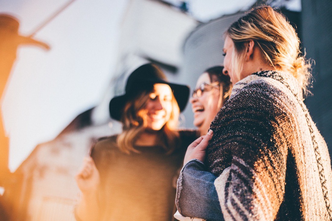 Three friends laughing together in warm golden afternoon light